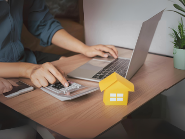 A person sitting at a table with a laptop and documents, reviewing mortgage options for buying a home.